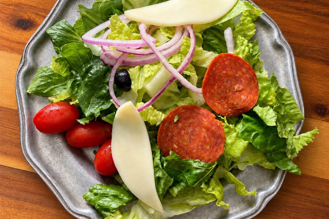 A fresh salad with romaine, tomatoes, red onion, pepperoni, mozzarella, and a black olive