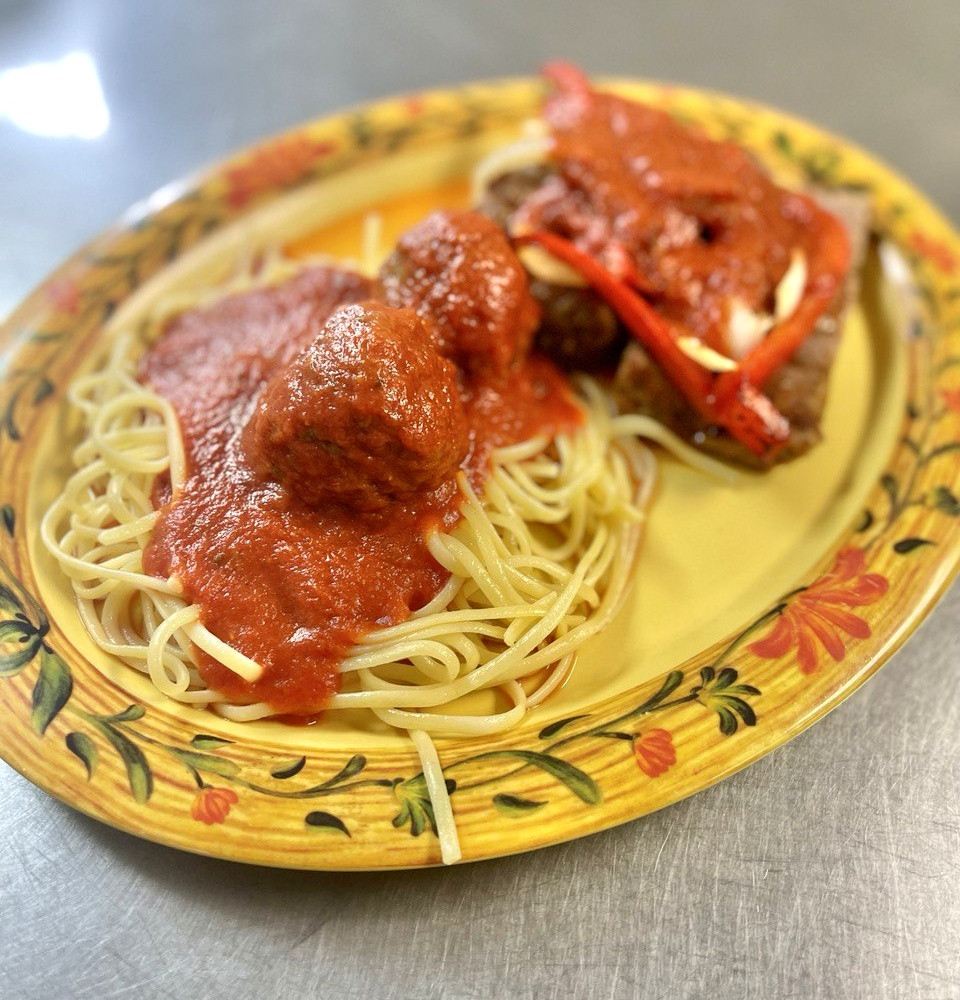 A yellow patterned plate with spaghetti, meatballs, and red sauce