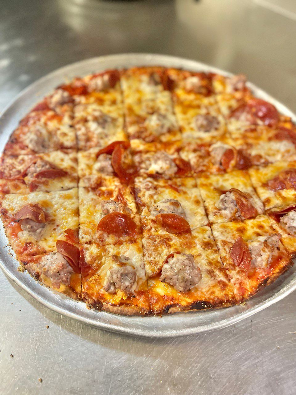 A thin crust pizza topped with pepperoni and sausage on a round metal tray