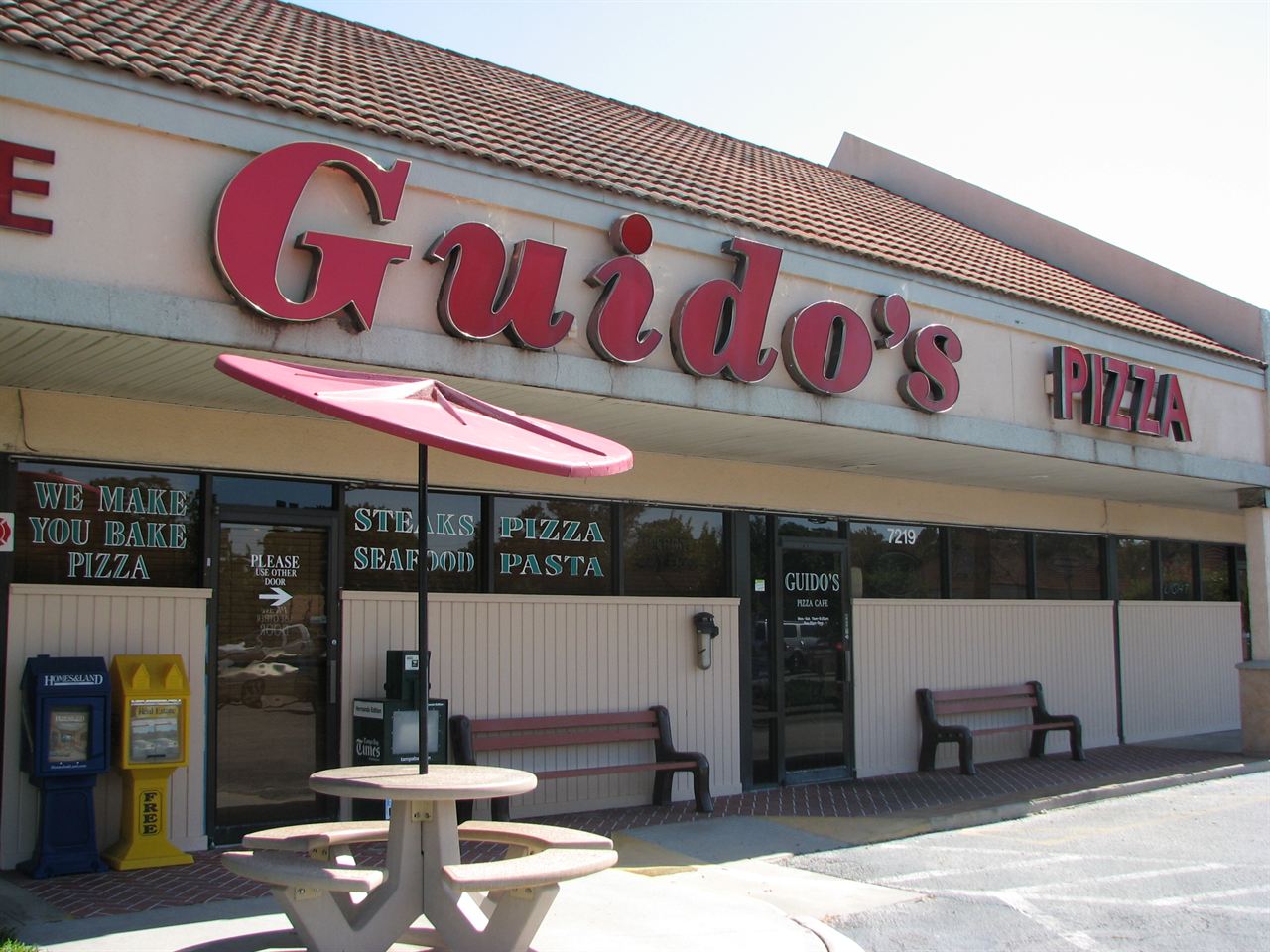 The front of Guido’s Pizza Cafe with the red Guido’s sign and outdoor table