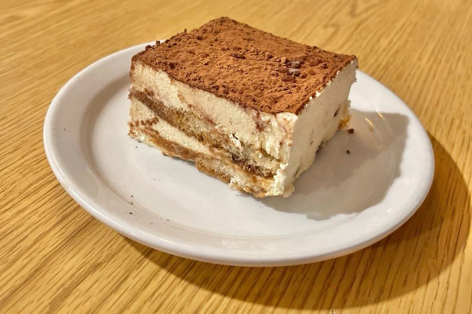 A square of tiramisu dusted with cocoa on a white plate
